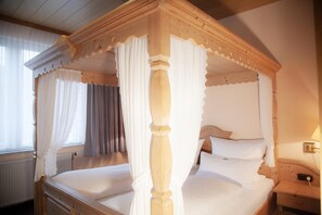 A four-poster canopy bed with white bedding, a wooden headboard, and a nightstand with a lamp.