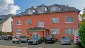 A multi-story hotel with a red facade, several windows, and a parking area with various cars. - Hotel Lonac (Duisburg)