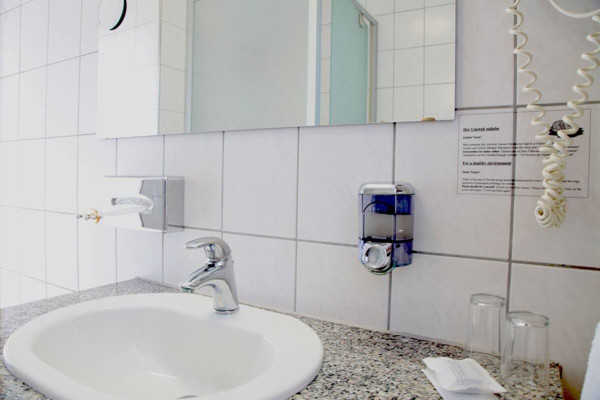Un baño con lavamanos blanco, espejo y dispensador de gel antibacterial.