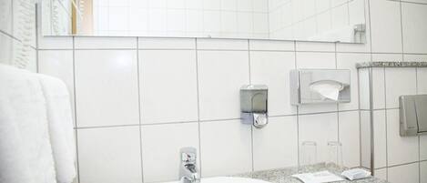 Un baño con un lavamanos blanco, un espejo, un perchero y un dispensador de toallas de papel.