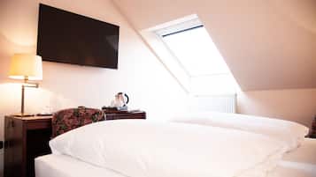 A bedroom with a bed, a desk with a lamp, a flat-screen TV, and a window.
