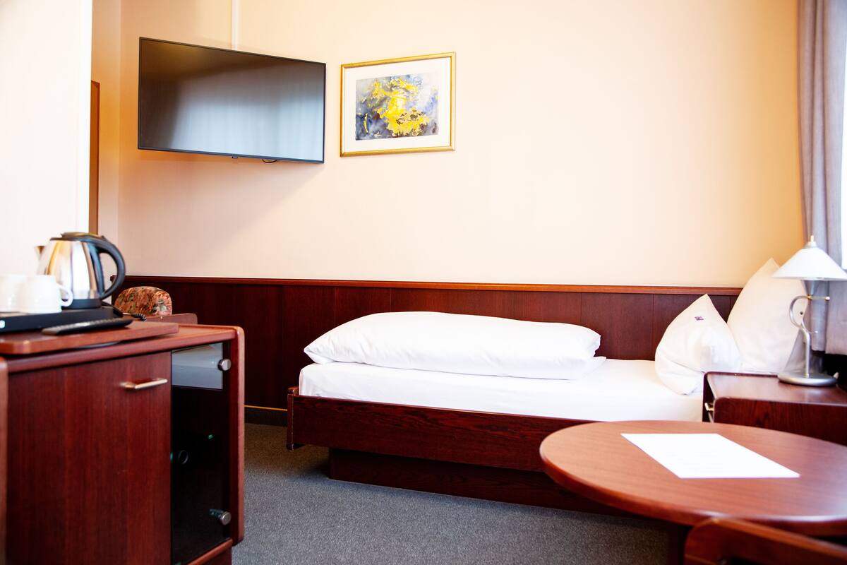 Habitación de hotel con cama, escritorio con lámpara, televisor y una obra de arte enmarcada en la pared.