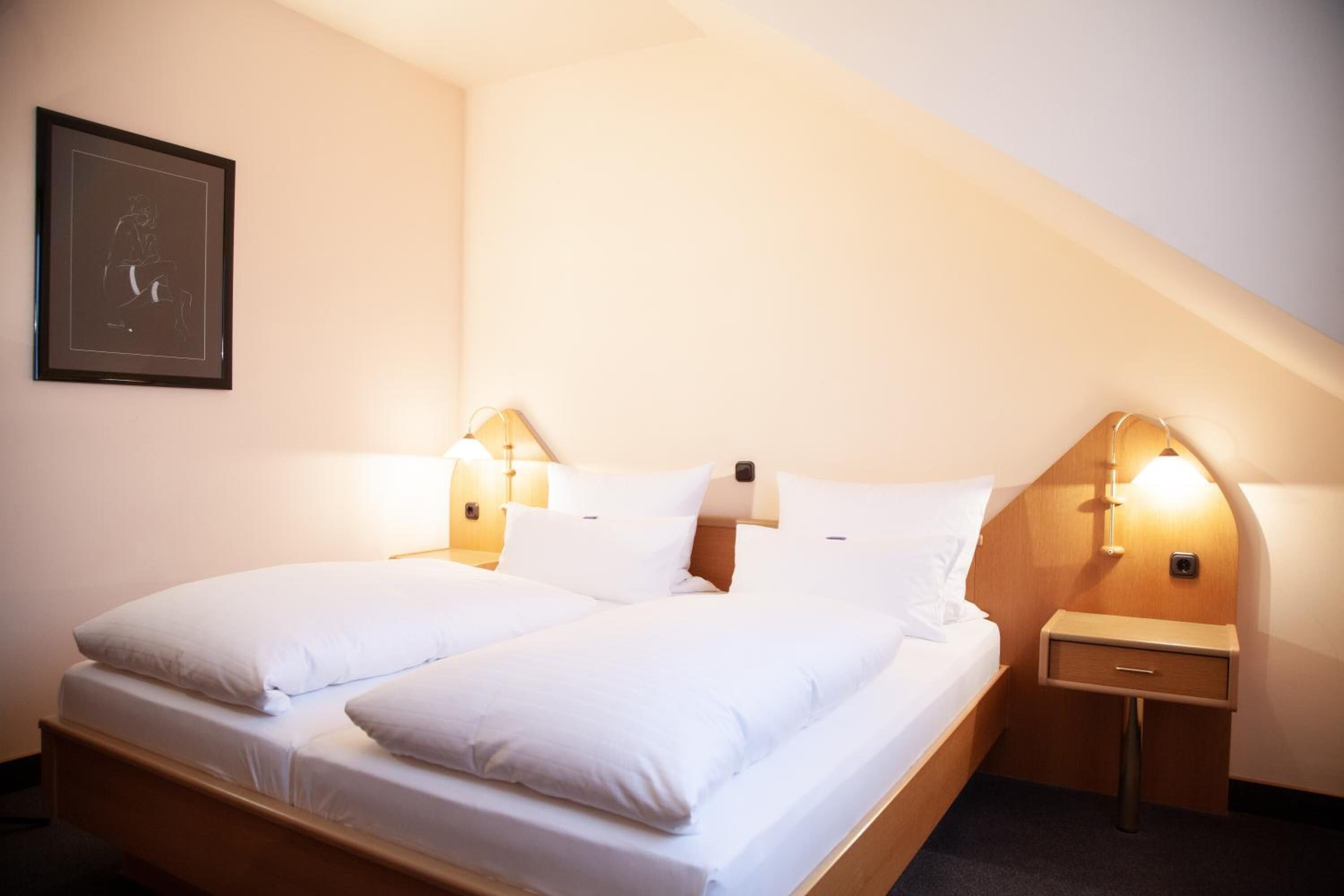 A twin bed with white linens in a room with a sloped ceiling.