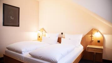 A twin bed with white linens in a room with a sloped ceiling.