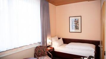A hotel room with a bed, a chair, a table, a lamp, and a framed picture on the wall.