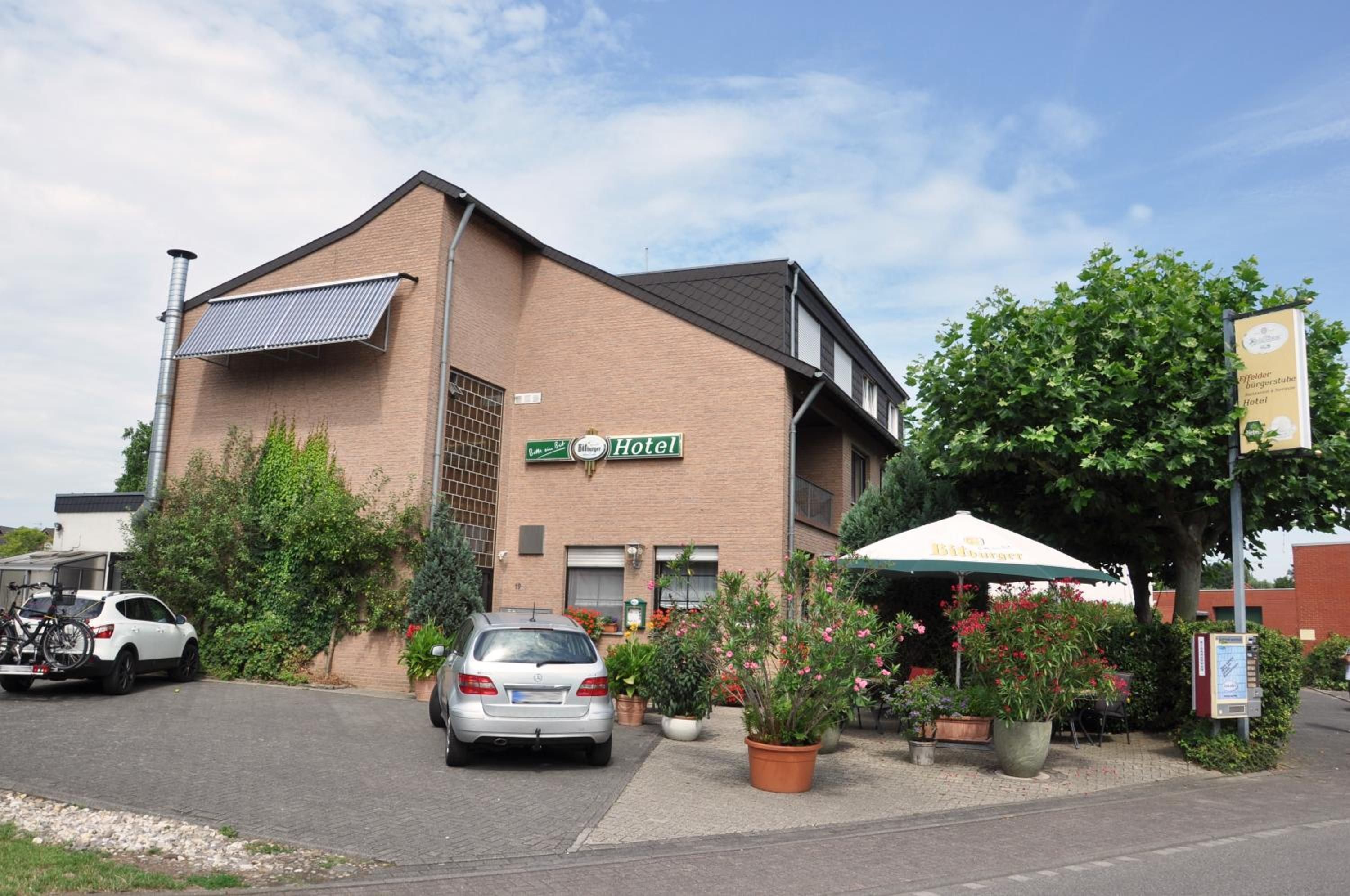 Un hôtel à la façade en briques, doté d’un espace extérieur couvert avec des sièges, et une voiture garée devant.