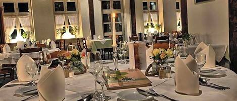 A dining area with round tables set for a meal, featuring white tablecloths, glassware, and floral centerpieces.