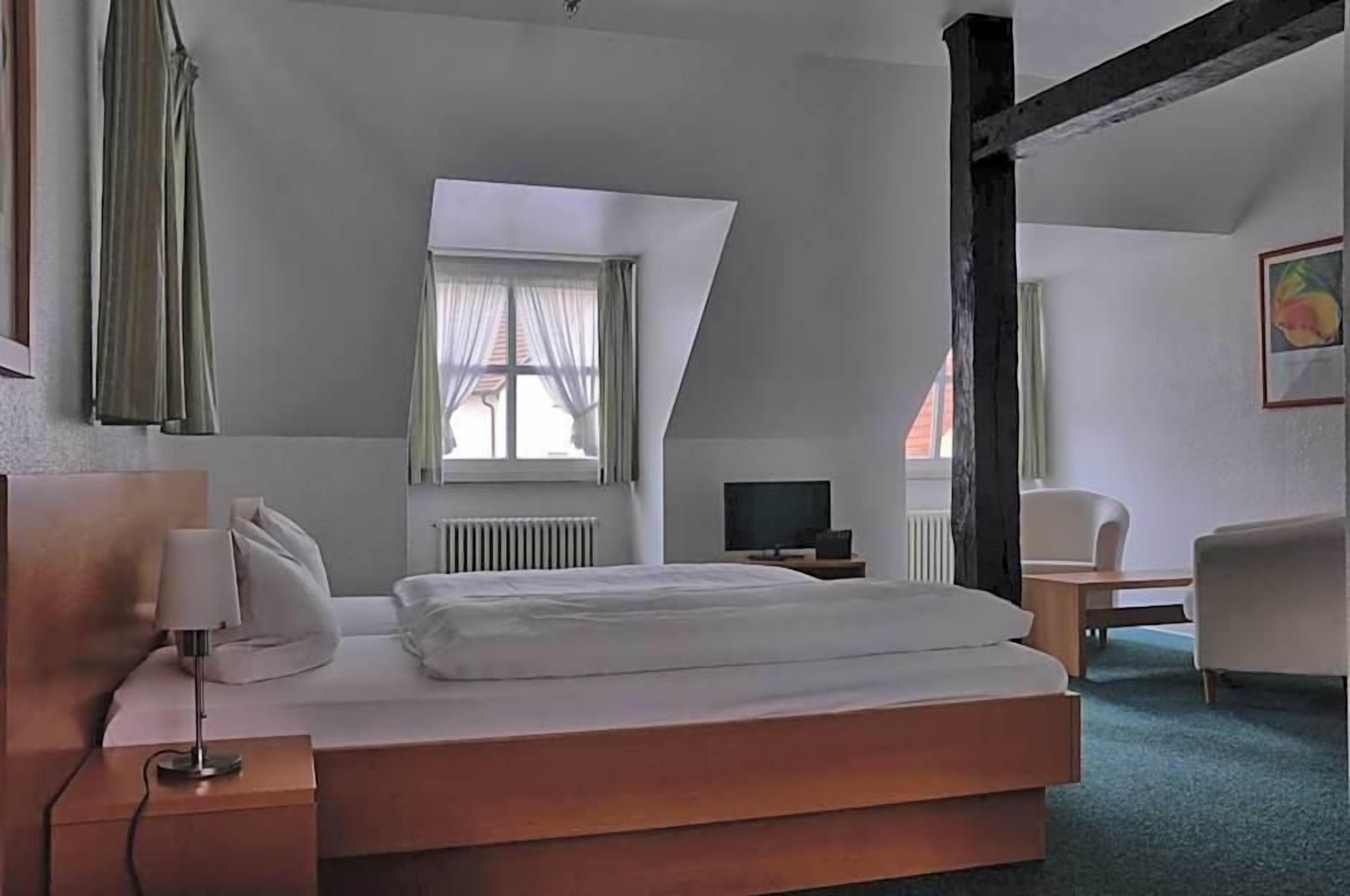 A hotel room with a bed, a TV, a chair, and a window with curtains.