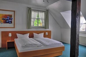 Een slaapkamer met een groot bed, een nachtkastje, een schilderij, een raam met gordijnen en een schuin dak.