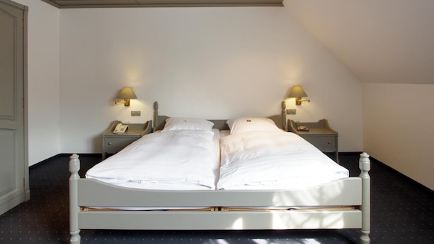 A double bed with two bedside tables, each with a lamp, in a room with a sloped ceiling and a black floor. - Flair-goldener Stern (Ascheberg)