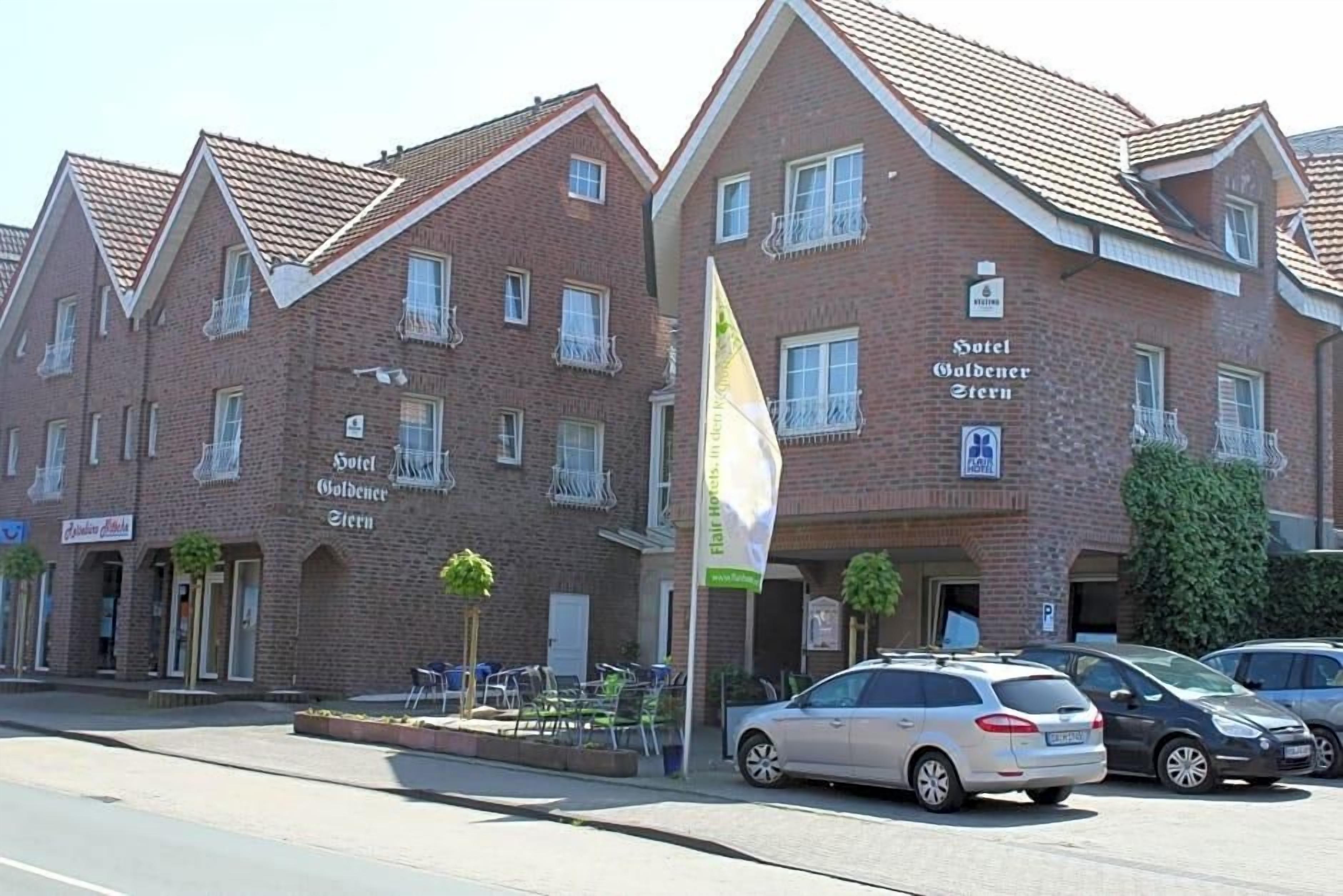 A hotel with a brick facade, multiple windows, and a flag. There are cars parked in front.