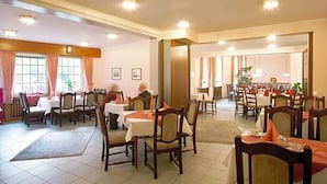 A hotel dining area with multiple tables and chairs, a large window with curtains, and a plant in the corner. - Flair-goldener Stern (Ascheberg)