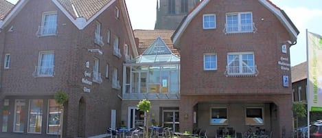 A traditional brick building with a central glass structure, possibly a cafe or restaurant, and a clock tower in the background.
