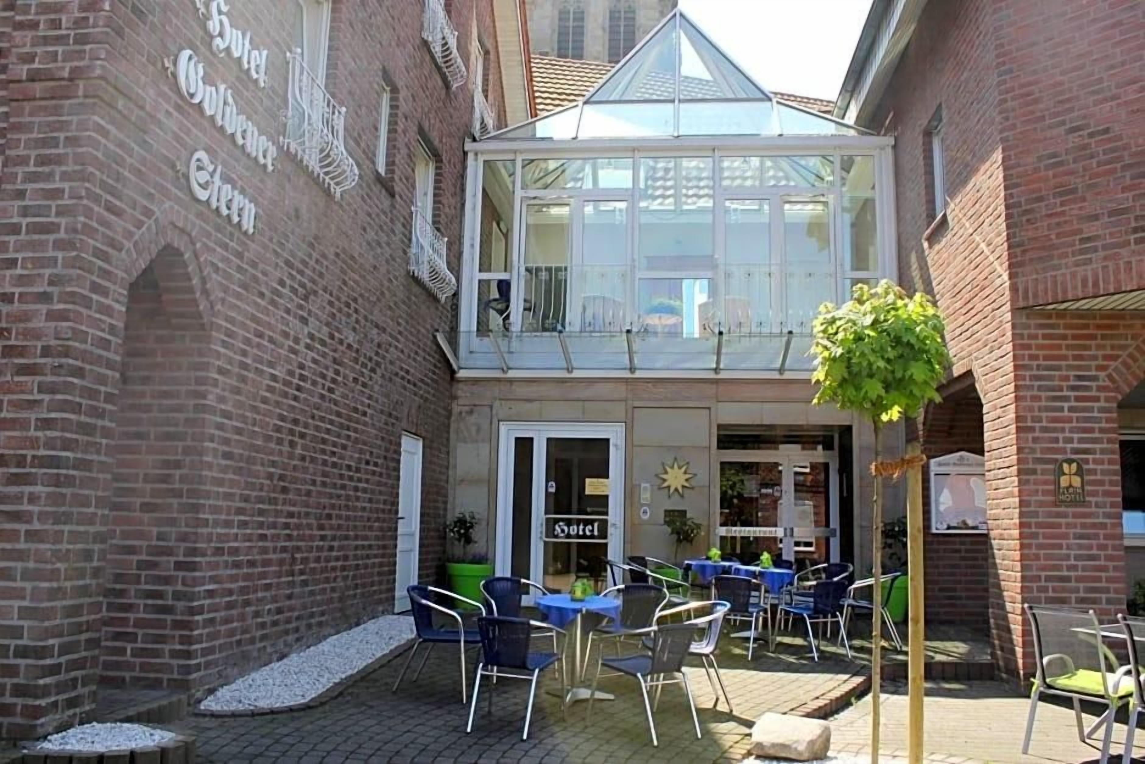 Un hôtel doté d’une véranda en verre, d’un espace extérieur aménagé pour s’asseoir et d’une façade en briques.