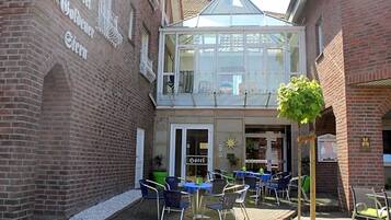 A hotel with a glass conservatory, outdoor seating area, and a brick facade.