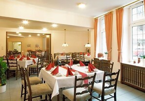 A dining area with tables set for service, chairs, and pendant lighting.