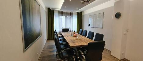A conference room with a long table, black chairs, a projector, and a clock on the wall.