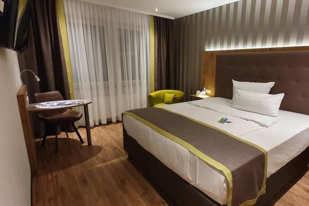Ett hotellrum med en stor säng, ett skrivbord, en stol och ett nattduksbord.