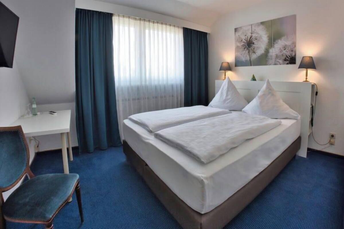 Ett hotellrum med en säng, ett skrivbord, en stol och ett fönster med gardiner.