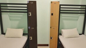 Deux lits simples avec des têtes de lit en bois, chacun portant un numéro sur le côté, dans une pièce aux murs de couleur claire et au sol carrelé.