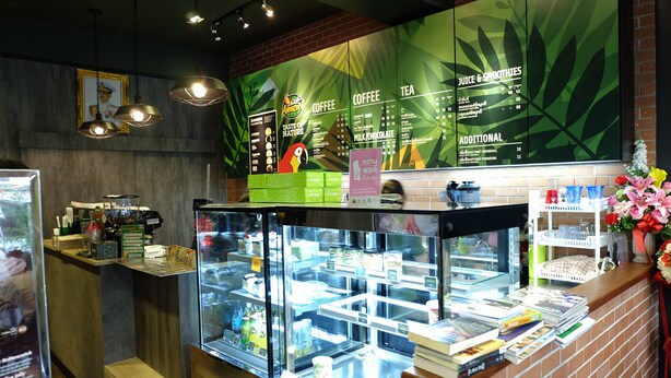 L’intérieur d’un café, avec un tableau affichant le menu, une vitrine remplie de livres et un comptoir où se trouve une machine à café.