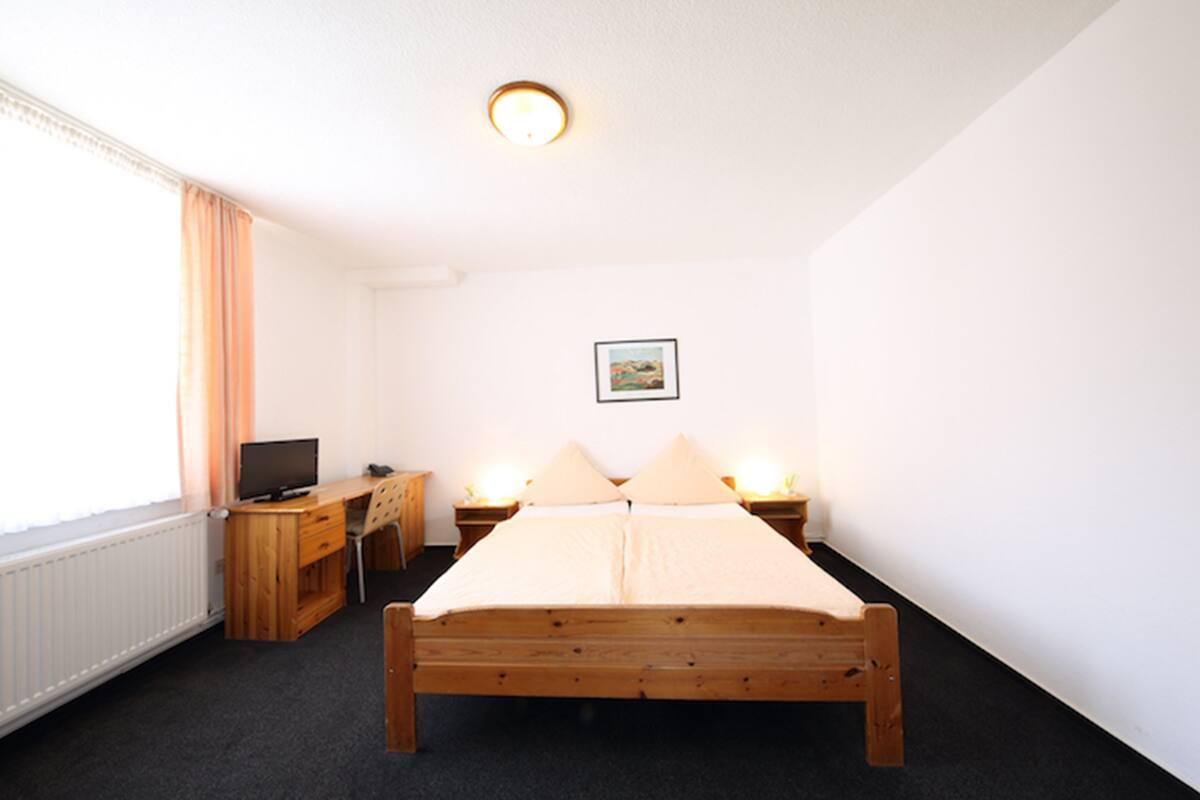 A bedroom with a wooden bed, a desk with a chair, a television, and two bedside lamps.