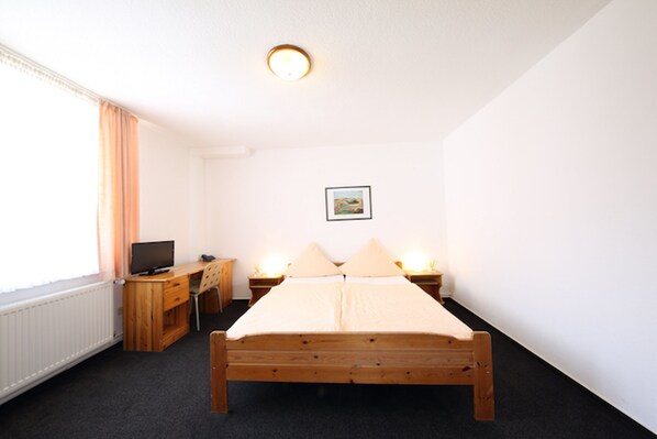 Un dormitorio con una cama de madera, un escritorio con silla, un televisor y dos lámparas de noche.