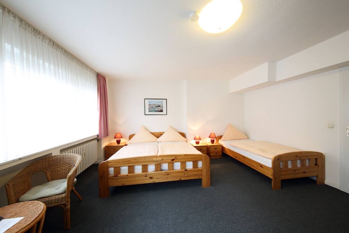 A room with two wooden beds, a wicker chair, a small table, and a radiator.