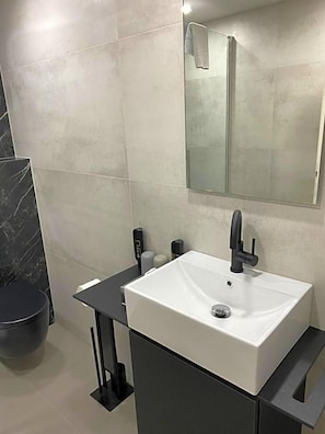 Une salle de bain moderne avec un lavabo blanc, un plan de toilette noir et un miroir au-dessus.
