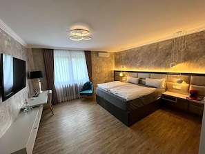 A modern hotel room with a large bed, a flat-screen TV, a desk, and a comfortable seating area.