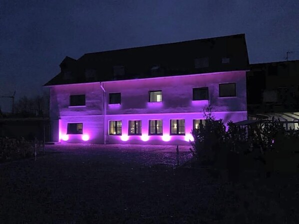 A building with multiple windows and a flat roof, illuminated by purple lighting.