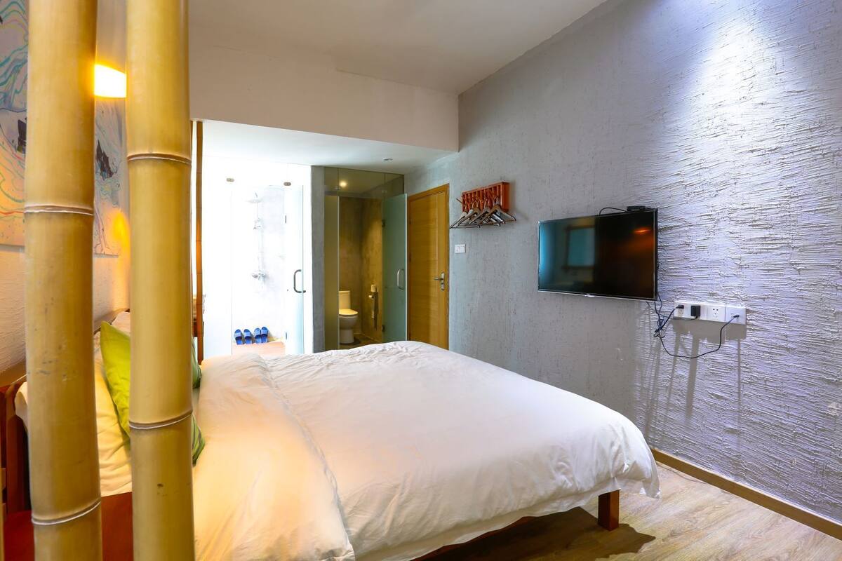 Ein Hotelzimmer mit Bett, einem an der Wand befestigten Fernseher und einem durchgegangenen Badezimmer.
