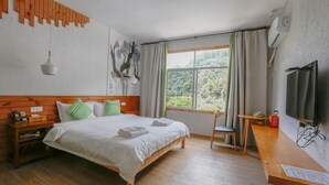 Ein Hotelzimmer mit einem hölzernen Bett, einem Schreibtisch, einem Stuhl, einem Fernseher und einem Fenster mit Vorhängen.