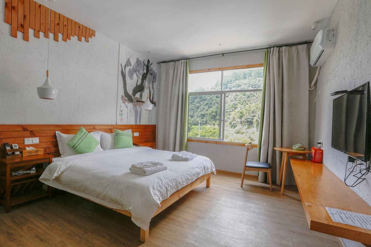 Ein Hotelzimmer mit einem hölzernen Bett, einem Schreibtisch, einem Stuhl, einem Fernseher und einem Fenster mit Vorhängen.