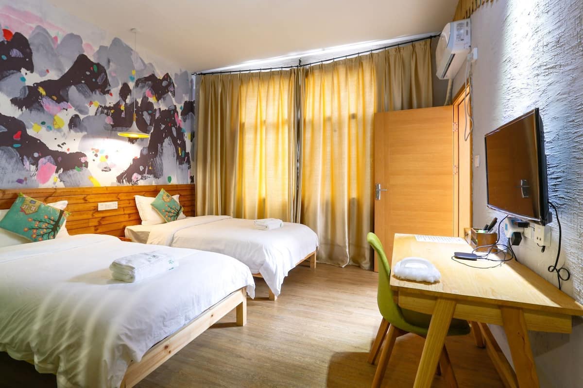 Ein Hotelzimmer mit zwei Betten, einem Schreibtisch mit Stuhl, einem Fernseher und einem großen, abstrakten Gemälde an der Wand.