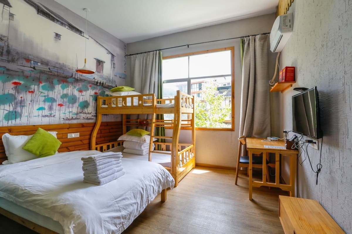 Ein Zimmer mit einem Etagenbett, einem Schreibtisch mit Computer, einem Fernseher und einem Fenster mit Vorhängen.