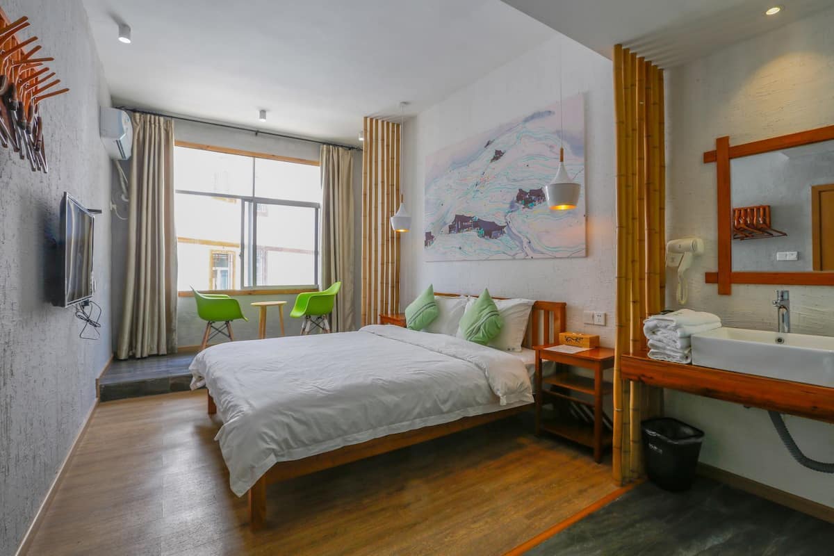 Ein modernes Hotelzimmer mit Bett, Schreibtisch, Stuhl, Bad mit Waschbecken und einem großen Fenster.