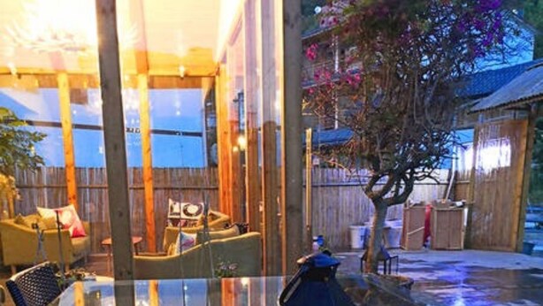 Eine gläserne Veranda mit Holzterrasse, Gartenmöbeln und einer Laterne.