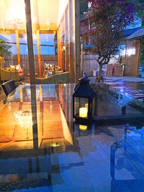 A glass-enclosed patio with a wooden deck, outdoor furniture, and a lantern. - Bajie Youth Hostel National Forest Park (Zhangjiajie)