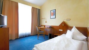 A hotel room with a bed, a desk, a chair, a television, and a window with curtains. - Birkenfelder Hof (Birkenfeld)