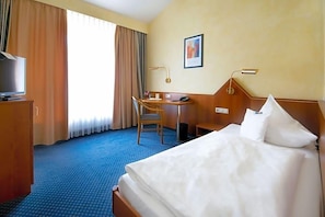 A hotel room with a bed, a desk, a chair, a television, and a window with curtains. - Birkenfelder Hof (Birkenfeld)