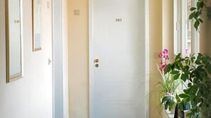 A hallway with a blue carpet, a white door labeled '301', and a potted plant with pink flowers. - Birkenfelder Hof (Birkenfeld)