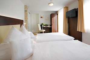 A hotel room with a bed, a desk, a chair, a TV, and a stone wall. - Birkenfelder Hof (Birkenfeld)