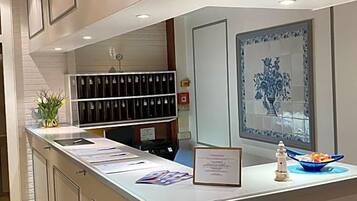 Un área de recepción con mostrador, un jarrón decorativo, un certificado enmarco y una ventana con diseño azul y blanco.