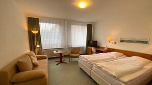 A hotel room with a bed, a desk, a chair, and a sofa.