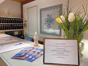 Un comptoir d’accueil agrémenté d’une pancarte de bienvenue encadrée, d’un vase rempli de fleurs et d’une petite maquette de phare.