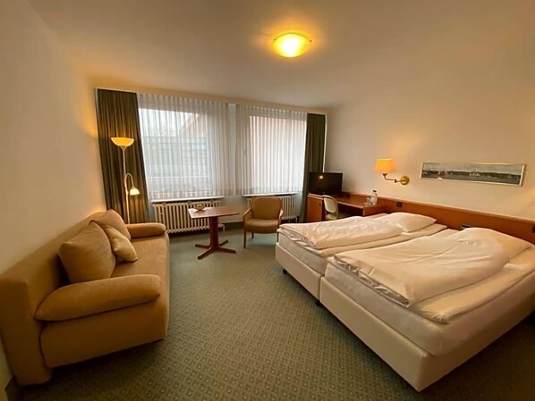 Une chambre d’hôtel avec un canapé, un bureau, deux lits, une chaise et un radiateur.