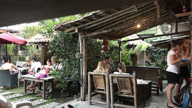 Un espace extérieur aménagé en terrasse, avec des tables et des chaises, entouré de verdure et agrémenté d’une pergola en bois.