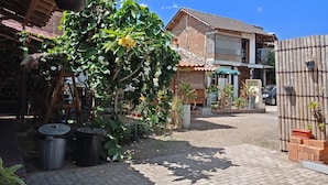 Une cour avec un bâtiment en briques, des plantes en pot et une clôture en bambou.