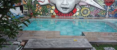 A swimming pool with a mural on the wall, surrounded by a wooden deck and stone tiles.